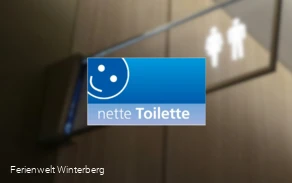 Ein verschwommenes Bild eines Toilettenschildes mit dem Logo für die nette Toilette in Winterberg im Vordergrund. Dieses Bild dient als Symbolbild für öffentliche Toiletten.